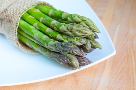 Bunch of fresh asparagus on wooden table and white plate, healthy foodの写真素材