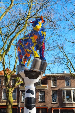 Delft, Netherlands - April 8, 2016: Colorful cow sculpture and traditional dutch houses on the square in downtown of popular Holland destination Delftのeditorial素材