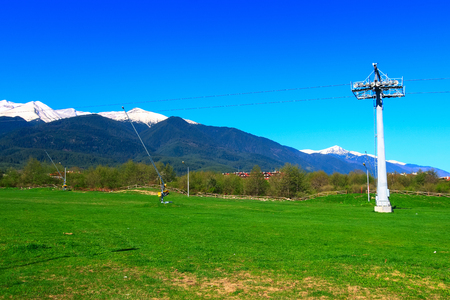 Spring landscape with green grass, chalet and snow mountain peaks of Pirin in ski resort Bansko, Bulgariaの写真素材