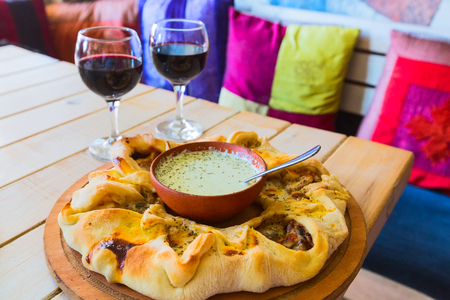 Traditional Georgian adjara round pie with sauce dressing, two wine glasses and sofa with pillowsの写真素材