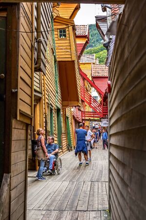 Bergen, Norway - July 30, 2018: City street view with Bryggen hanseatic league houses with colorful facades and people walking along the shopsのeditorial素材