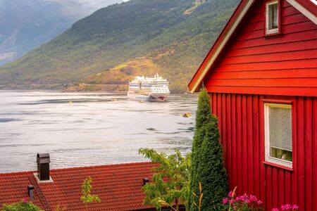 Flam, Norway - July 31, 2018: Norwegian fjord Sognefjord landscape, red wooden house and Aidaluna cruise shipのeditorial素材