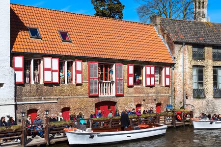 Bruges, Belgium - April 10, 2016: Scenic cityscape with medieval houses, cruise boat station with tourists and canalのeditorial素材