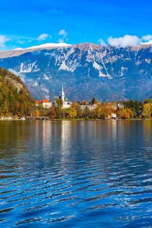 View of Lake Bled with Church, Slovenia. Autumn colorful trees and snow mountains backgroundの写真素材