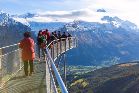 Grindelwald, Switzerland - October 10, 2019: People taking photos on sky cliff walk metal bridge at First peak of Swiss Alps mountain, snow peaks panorama, Bernese Oberland, Europeのeditorial素材