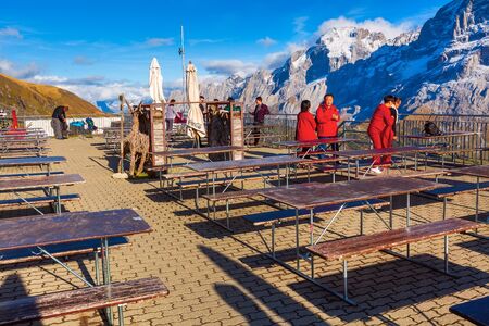 Grindelwald, Switzerland - October 10, 2019: People at the bar terrace on sky cliff walk metal bridge at First peak of Swiss Alps mountain, snow peaks panorama, Bernese Oberland, Europeのeditorial素材