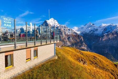 Grindelwald, Switzerland - October 10, 2019: People at the bar terrace on sky cliff walk metal bridge at First peak of Swiss Alps mountain, snow peaks panorama, Bernese Oberland, Europeのeditorial素材