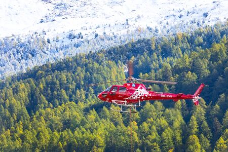 Zermatt, Switzerland - October 7, 2019: Zermatt air red helicopter and pine treesのeditorial素材