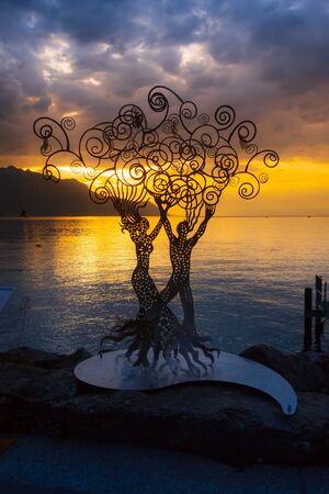 Montreux, Switzerland metal figure of a woman and man at promenade of Geneva Lake, colorful blue and yellow sunsetのeditorial素材
