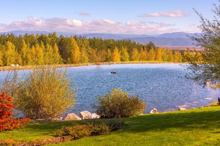 Beautiful autumn landscape view of the lake, pine trees, wooden chalets and mountains background near Bansko, Bulgariaの写真素材