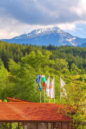 Bulgaria, Bansko - May 5, 2020: Hotel flags, green forest and Todorka mountain summer viewのeditorial素材