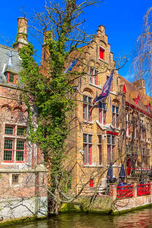 Bruges, Belgium - April 10, 2016: Scenic cityscape with medieval houses, cafe with tourists and canal in Bruggeのeditorial素材
