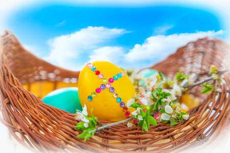 Easter basket with colorful eggs on blue cloudy sky, tree flower branch, close-up, holiday card
