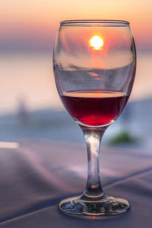 Romantic glass of wine. Sunset on beach reflected in red wine, summertime vacation conceptの写真素材