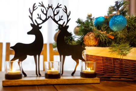 Reindeer christmas toy on wooden table, candle lights, green branch, pine cones holiday interiorの写真素材
