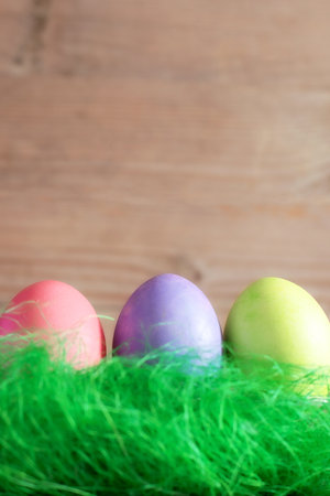 Colorful Easter eggs in green grass nest on wooden background copy space
