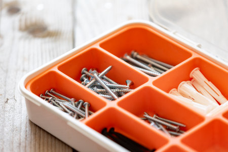 Collection of nails, thumb nails, screws, plastic and bolts in plastic box on the wooden table