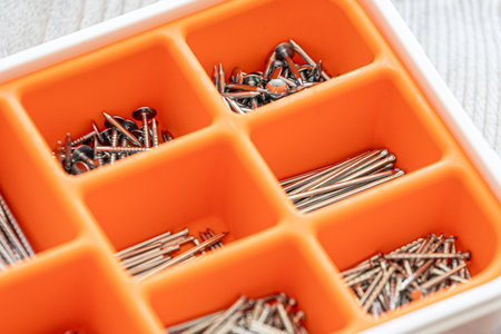 Collection of nails, thumb nails, screws, plastic and bolts in plastic box on the wooden table