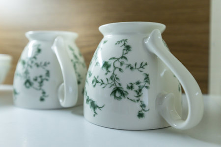 Set of clean mugs upside down in opened white and wooden kitchen cupboard shelf, storage cabinetの写真素材