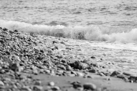 Pebbles on the seashore close-up. Rocky beach stones, sea water waves natural background, black and whiteの写真素材