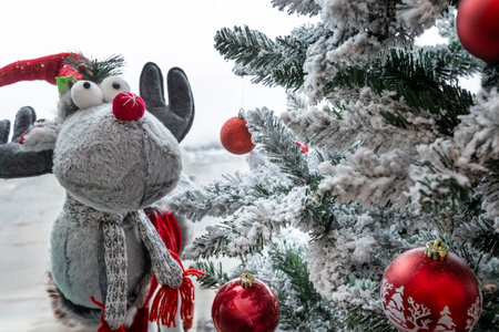 Christmas tree with snow branches, ball decorations and figurine of cute Reindeer Toy. Window with winter viewの写真素材