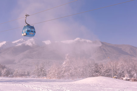 Bansko, Bulgaria - December 5, 2019: Winter ski resort panorama with blue gondola lift cabins, forest pine trees, Pirin mountain peaks view and slopeのeditorial素材