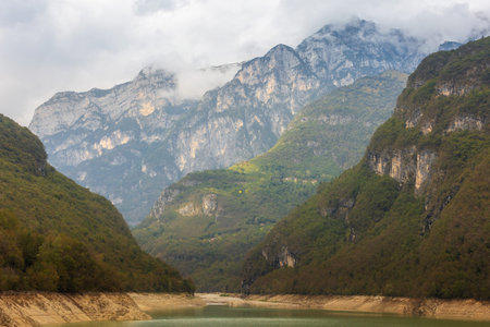 Mountain lake near Cadini del Brenton surrounded by cliffs, forested slopes and misty peaks, Dolomites, Italyの写真素材