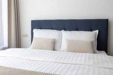 Elegant double bed with navy blue tufted headboard white striped linens and textured beige pillows