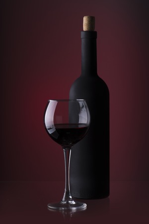 Pouring red wine into the glass against wooden backgroundの写真素材