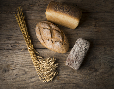 Bread border on wood with copy space background. Brown and white whole grain loaves still life composition with wheat ears scattered around. Bakery and grocery food store concept.の写真素材