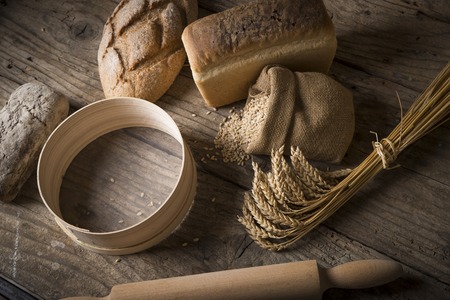 Bread border on wood with copy space background. Brown and white whole grain loaves still life composition with wheat ears scattered around. Bakery and grocery food store concept.の写真素材