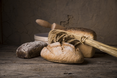 Bread border on wood with copy space background. Brown and white whole grain loaves still life composition with wheat ears scattered around. Bakery and grocery food store concept.の写真素材