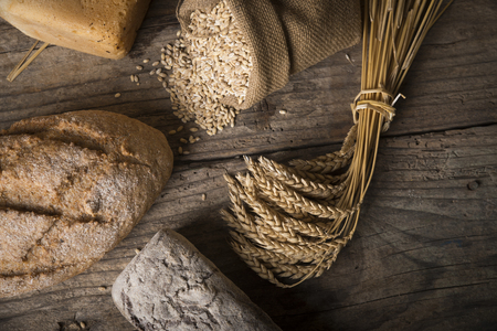 Bread border on wood with copy space background. Brown and white whole grain loaves still life composition with wheat ears scattered around. Bakery and grocery food store concept.の写真素材