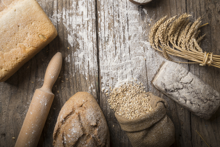 Bread border on wood with copy space background. Brown and white whole grain loaves still life composition with wheat ears scattered around. Bakery and grocery food store concept.の写真素材