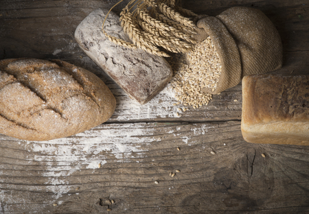 Bread border on wood with copy space background. Brown and white whole grain loaves still life composition with wheat ears scattered around. Bakery and grocery food store concept.の写真素材