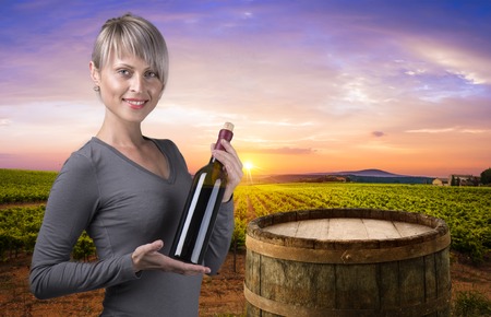 Young barefoot girl holding straw basket with a bottle of wine over natural backgroundの写真素材