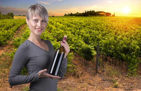 Young barefoot girl holding straw basket with a bottle of wine over natural backgroundの写真素材