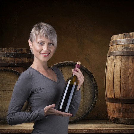 Young barefoot girl holding straw basket with a bottle of wine over natural backgroundの写真素材