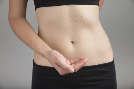 Slim and fit woman holds her hands on belly. Isolated on white.