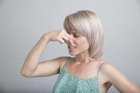 Female gesture smells bad. Portrait of woman wearing casually pinches nose with fingers hands looks with disgust something stinks bad smell situation. Human face expression body language reactionの写真素材