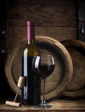 Pouring red wine from bottle into glass with wooden wine casks on backgroundの写真素材