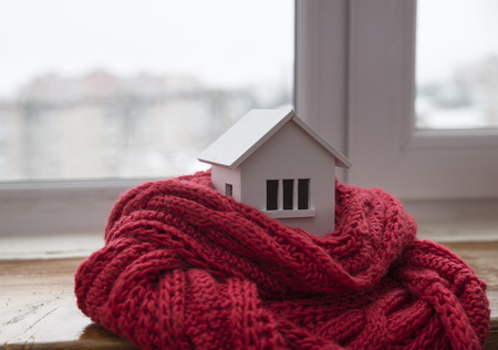 house in winter - heating system concept and cold snowy weather with model of a house wearing a knitted cap