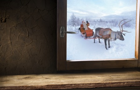 Christmas background. A cup of tea, books, a candle and a knitted scarf on the window background. Outside the window is winter, snowfall and Christmas tree lights. Cozy warm home holiday atmosphere.の写真素材