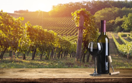 Red wine bottle and wine glass on wodden barrel. Beautiful Tuscany background