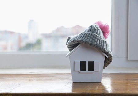house in winter - heating system concept and cold snowy weather with model of a house wearing a knitted capの写真素材