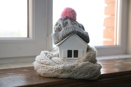 house in winter - heating system concept and cold snowy weather with model of a house wearing a knitted capの写真素材
