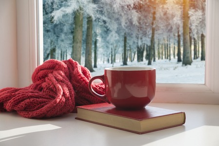 Cup of hot coffee and cozy knitted scarf on wooden table in front of glitter background with snowflakes overlayの写真素材