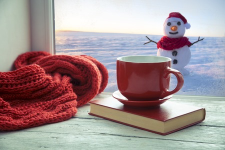 Cup of coffee on the window sill. In the background, a beautiful winter landscape in snow. Cozy home conceptの写真素材