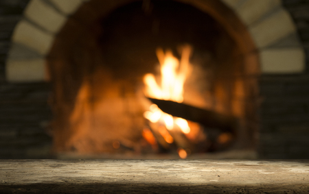 Old wooden table and fireplace with warm fire on the background.の写真素材