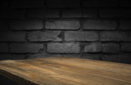 Old wood table with blurred concrete block wall in dark room background.の写真素材
